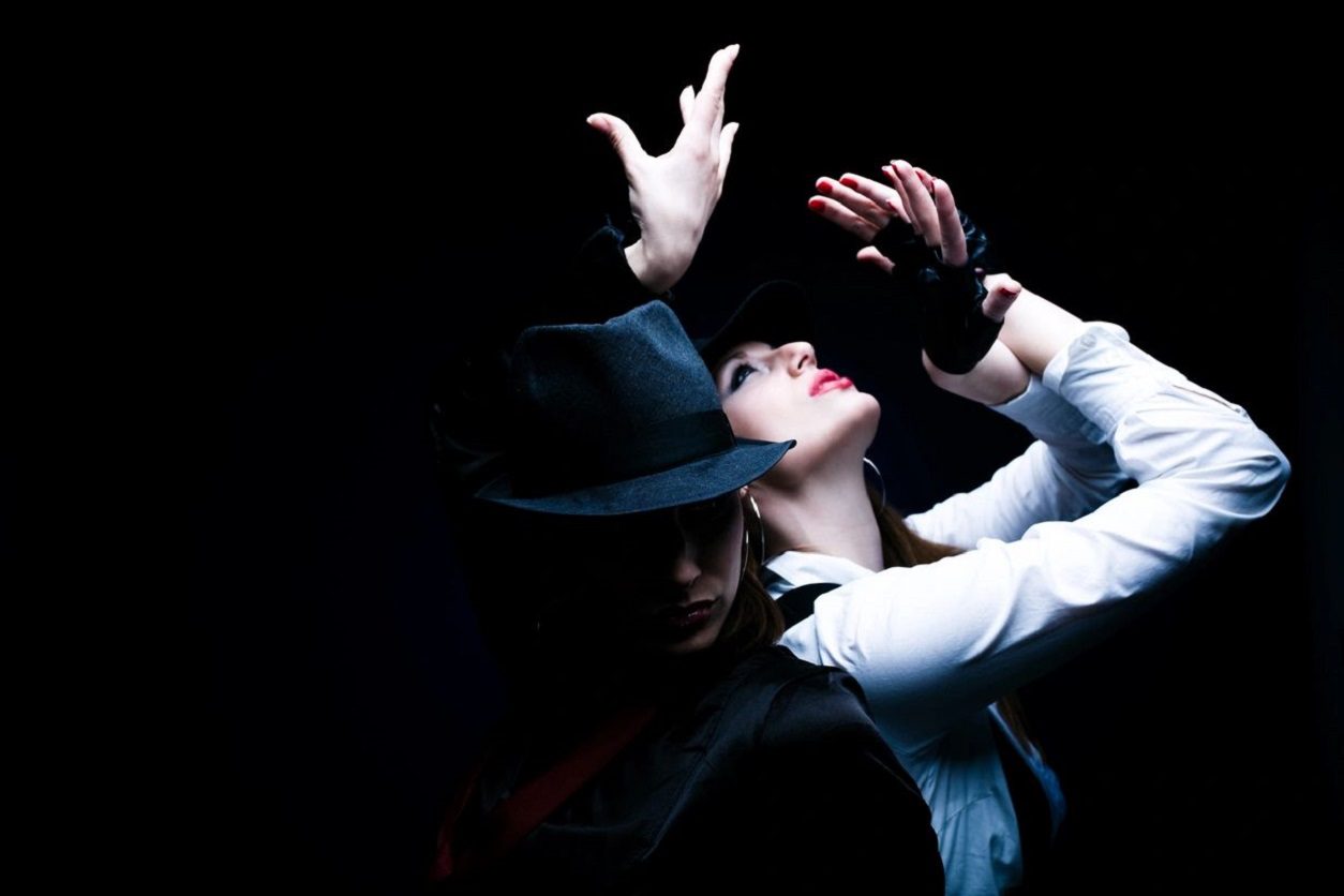 A man and woman in black hats dance.