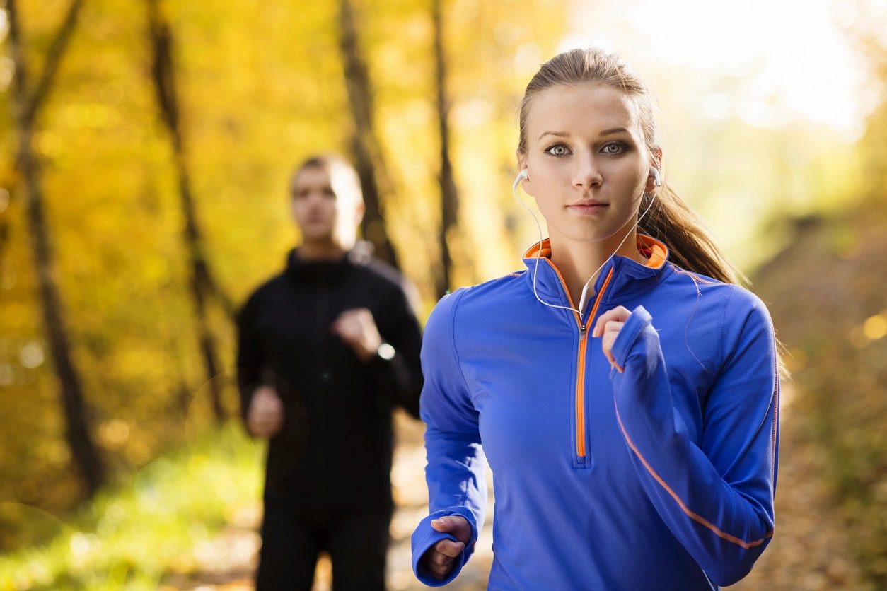 A woman running in the woods while wearing headphones.