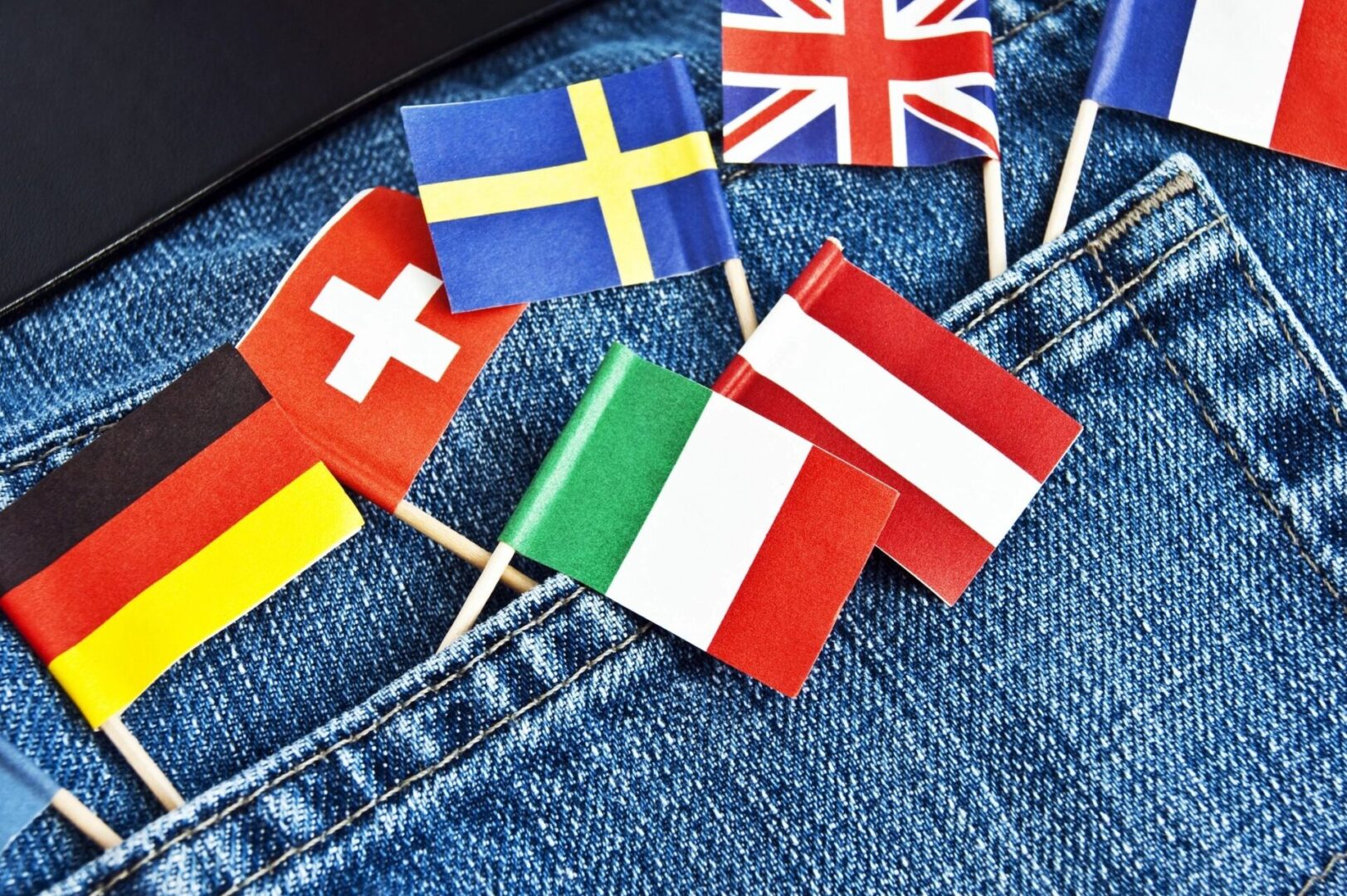 A bunch of small flags of different country in the back pocket of a jeans.